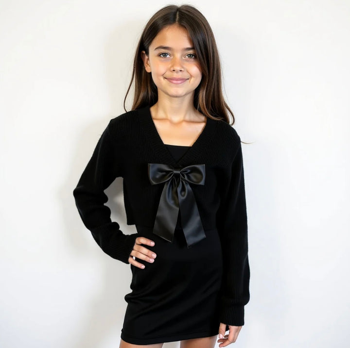 Young girl wearing a black dress with Gold Rush NYC’s Black Addison Satin Bow Sweater on a white background